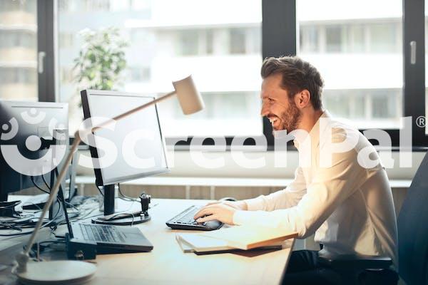 Man In White Dress Shirt Sitting On Black Rolling Chair While Facing Black Computer Set And Smiling